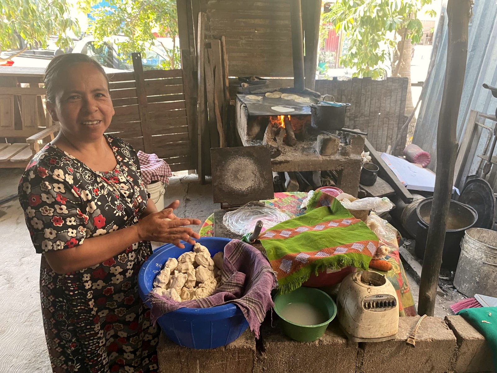 Cook preparing nixtamal masa over a wood-fired comal